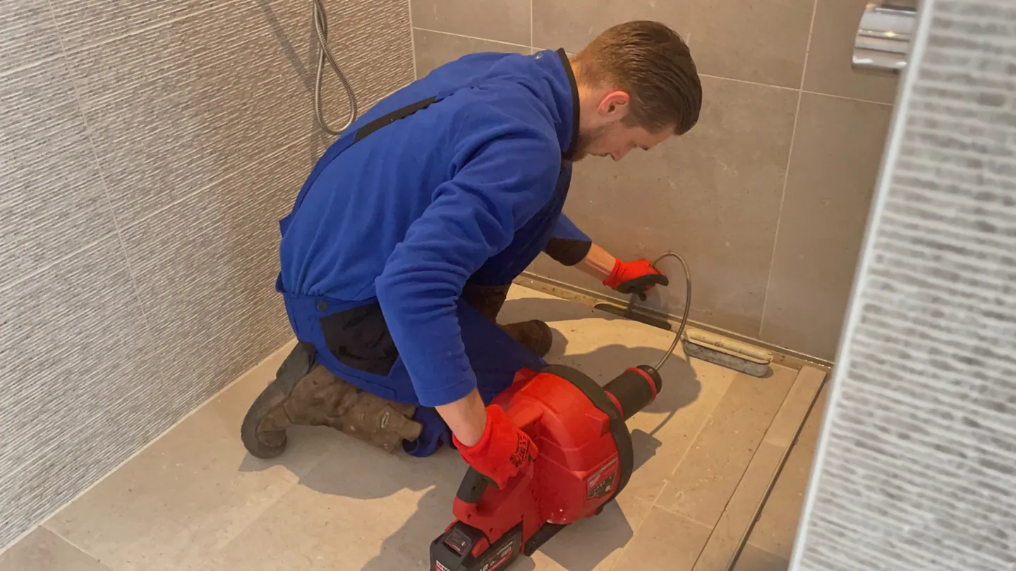 Monteur ontstopt een doucheafvoer en douchegoot met een ontstoppingsmachine